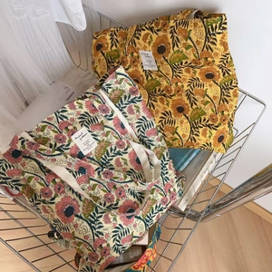 Detail of floral printed cotton tote bags in yellow and pink on a metal shelf