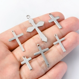 Assorted silver stainless steel cross pendants in six sizes held in hand for DIY jewelry