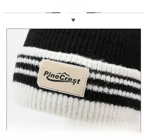 Détail du bonnet en tricot rayé noir et blanc avec un écusson de marque en cuir brun