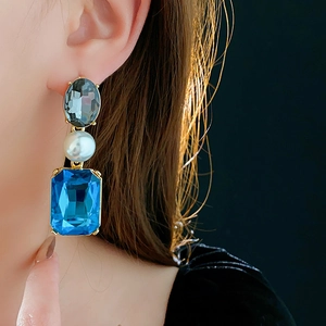 Close-up of vintage gold earrings with blue gemstones and white pearls on a model
