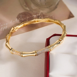 18K gold-plated bamboo joint bangle with cubic zirconia crystals next to a red jewelry box