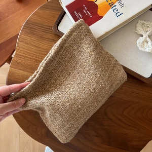 Chic beige wool tweed makeup bag with zipper closure on a cozy wooden desk setting