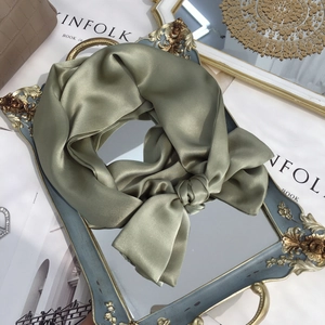 Close-up of a sage green pure silk scarf tied in a bow on a vintage gold tray