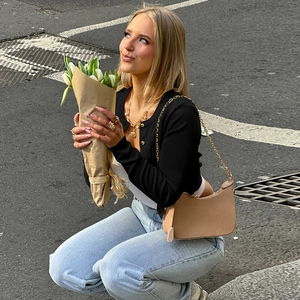 Détail d'un gilet noir en maille ajusté avec boutons métalliques et sac à bandoulière