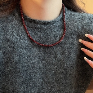 Close-up of deep red gravel beaded necklace styled on a grey knitted wool sweater