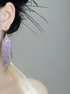 Detail of long fringe earrings featuring purple tassels and shimmering crystals on a model