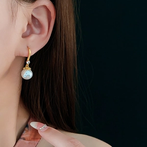 Detail of elegant 14K gold-plated earring with white pearl and sparkling zircon on ear