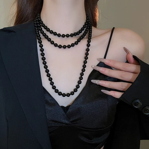 Detail view of multi-layered black pearl necklace on a model in elegant dark attire