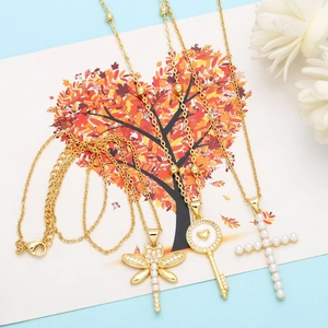 Three-piece gold necklace set featuring dragonfly, heart key, and pearl cross charms