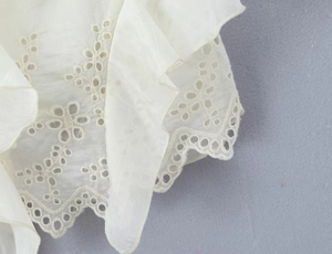 Detail of white cotton lace fabric featuring delicate hollow embroidery and ruffled edges
