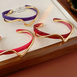 Detail view of gold-plated geometric bracelets in purple, dark red, and rose pink enamel
