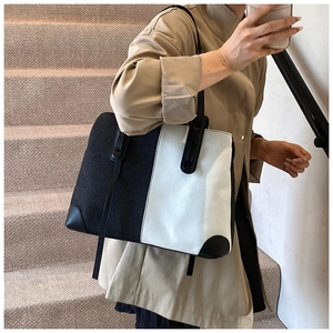 Detail of large black and white patchwork tote bag with leather handles and corner protectors