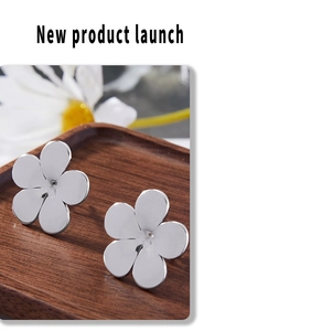 Close-up of silver flower stud earrings on a dark wood tray with a floral background