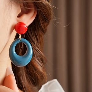 Close-up of model wearing geometric resin earrings with red button and blue ring design