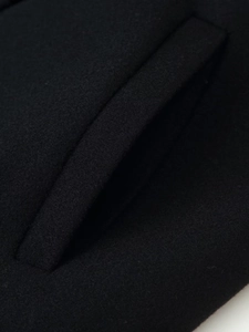 Détail d'une poche passepoilée en biais sur un manteau noir en laine de haute qualité