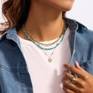 Detail shot of a layered gold necklace set with turquoise beads and a heart pendant