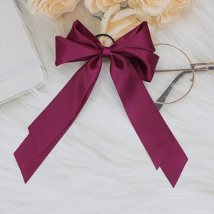 Close-up of wine red satin ribbon bow hair scrunchie on soft white plush background