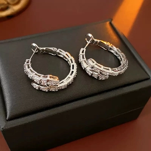 Detail of silver snake-pattern hoop earrings with clear zircons on black jewelry box