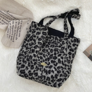 Close-up of leopard print faux fur tote bag with golden metal logo on soft plush background