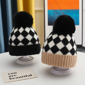 Detail of baby knit hat featuring black and white plaid pattern and fluffy faux fur pompom