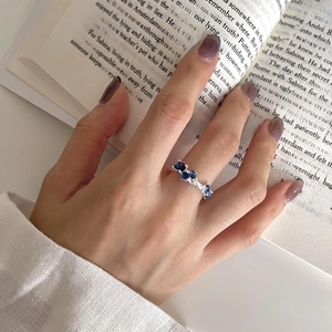 Irregular S925 silver ring with blue sapphire cluster crystals worn on finger over a book