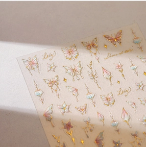 Close-up of holographic gold butterfly nail art stickers with elegant floral designs