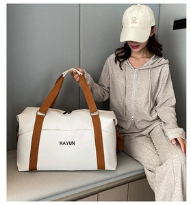 Detailed side view of a cream travel bag with brown straps held by a model