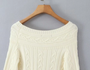 Gros plan du pull blanc cassé en maille torsadée avec boutons sur cintre en bois