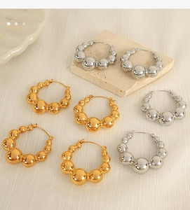 Detailed view of gold and silver beaded hoop earrings on a textured stone surface
