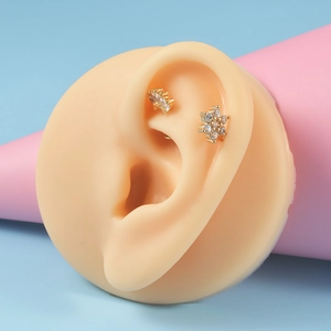 Macro detail of golden flower and curved zircon stud earrings on a silicone ear model