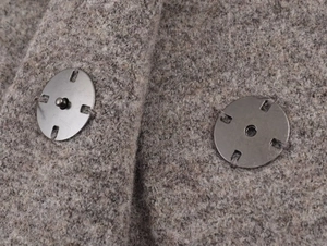 Macro shot of silver metal snap buttons on thick taupe knitted wool fabric of the jacket