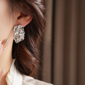 Close-up of irregular silver-toned crinkled earring with a molten liquid metal texture