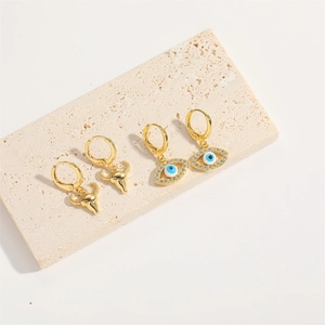 Detail of gold evil eye and bull head earrings featuring blue zircons on stone surface