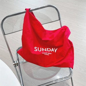 Detail of red canvas shoulder bag featuring white SUNDAY print on a modern chair