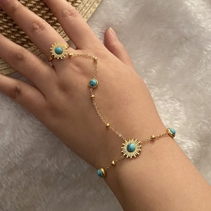 Détail d'une chaîne de main bohème dorée avec des perles turquoise sur un fond doux