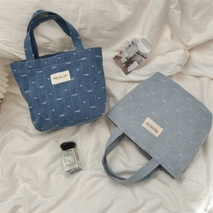 Détail de sacs fourre-tout en denim bleu avec broderie de nœuds blancs et cœurs
