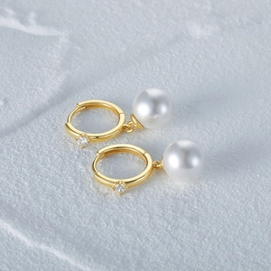 Detail of elegant gold hoop earrings with white pearl pendants and small zircon accents