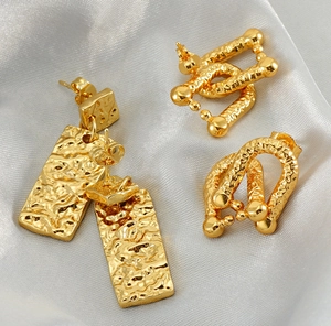 Macro shot of gold hammered rectangular earrings on grey silk fabric texture