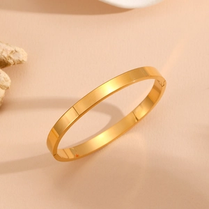 Detailed top view of a polished gold minimalist stainless steel bangle on a warm beige background