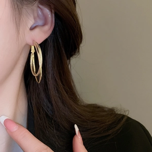Detailed close-up of textured gold layered hoop earring worn on model's ear
