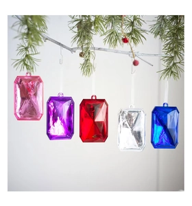 Close-up of five colorful acrylic gem ornaments hanging on a pine branch with red berries