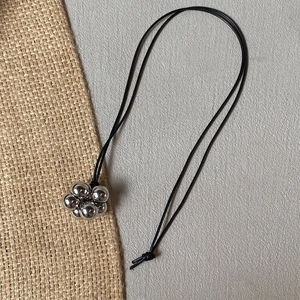 Detail of silver spherical flower pendant on black cord necklace with minimalist design