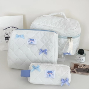 Three-piece set of white quilted cosmetic bags with blue bow ties and soft zipper handles
