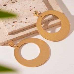 Macro detail of large gold geometric earrings with a brushed metal matte texture finish