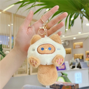 Close-up of plush cat keychain with blue eyes and gold metal clip on a backpack