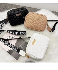 Close-up of wave-quilted crossbody bags in black, beige and white with printed straps