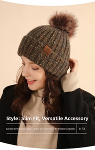 Detail of dark green knit beanie with fluffy brown pompom and snowflake leather patch