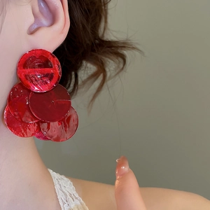 Close-up of red circular shell earrings with a glossy finish worn by a model