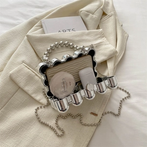 Silver metallic wave eggshell clutch bag with pearl handle and chain on a beige blazer