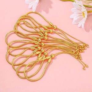 Detailed view of ten gold-toned snake chain bracelets with bead ends on a pink background